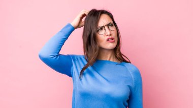 Genç, güzel bir kadın şaşkın ve kafası karışmış hissediyor, başını kaşıyor ve yan tarafa bakıyor.