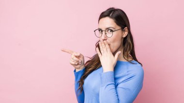 Genç, güzel bir kadın kendini mutlu, şok olmuş ve şaşırmış hissediyor. Ağzını eliyle kapatıyor ve yanal kopya alanını işaret ediyor.