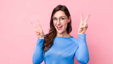 Genç ve güzel bir kadın gülümsüyor ve mutlu görünüyor, arkadaş canlısı ve memnun, işaret eden zafer ya da barış iki elle