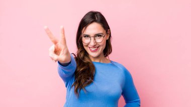 Genç ve güzel bir kadın gülümsüyor ve mutlu görünüyor, kaygısız ve pozitif, zafer ya da barış işareti yapıyor.