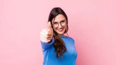 Genç, güzel bir kadın gururlu, tasasız, kendinden emin ve mutlu, başparmağıyla olumlu gülümsüyor.