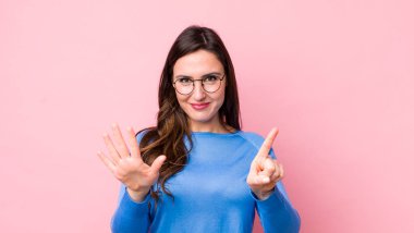 Genç, güzel bir kadın gülümsüyor ve arkadaş canlısı görünüyor. Altı ya da altıncı numarayı gösteriyor. Elleri önde, geri sayıyor.