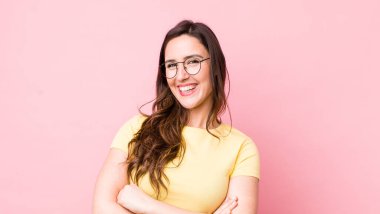 Genç ve güzel bir kadın kollarını kavuşturup mutlu bir şekilde gülüyor, rahat, pozitif ve tatmin edici bir pozla.