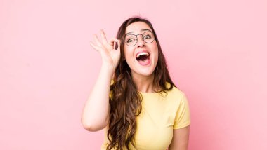 Genç ve güzel bir kadın kendini başarılı ve tatmin olmuş hissediyor, ağzı açık gülümsüyor, elle işaret veriyor.