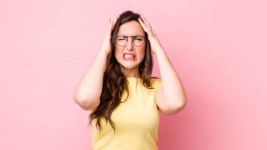 Genç ve güzel bir kadın stresli ve endişeli, depresif ve hayal kırıklığına uğramış hissediyor, iki elini de başa kaldırıyor.