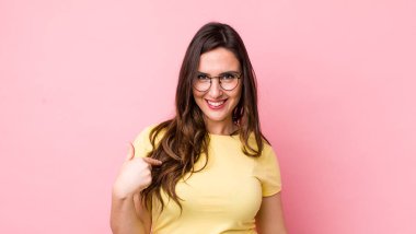 Genç ve güzel bir kadın gururlu, kendinden emin ve mutlu görünüyor, gülümsüyor ve kendini işaret ediyor ya da bir numaralı işareti yapıyor.