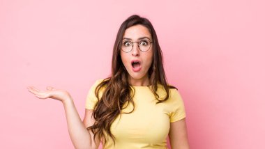 Genç ve güzel bir kadın şaşırmış ve şok olmuş görünüyor, çenesi düşmüş, bir objeyi elinde açık bir elle tutuyor.