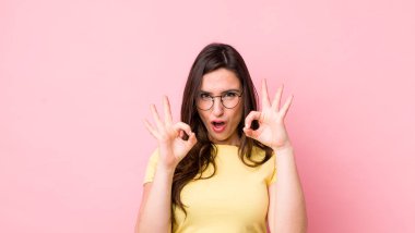 Genç, güzel bir kadın şok olmuş, şaşırmış ve şaşırmış hissediyor. İki eliyle de onay işareti yapıyor.