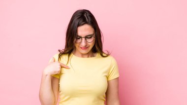 Genç ve güzel bir kadın neşeyle gülümsüyor, yere bakıyor ve göğsüne işaret ediyor.