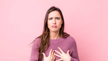 Genç ve güzel bir kadın, şaşkın ve şaşkın bir bakışla kendini işaret ediyor, seçildiğine şaşırmış ve şaşırmış.