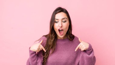 Genç, güzel bir kadın şoke olmuş, ağzı açık ve şaşırmış, inançsızlık ve şaşkınlık içinde bakıyor ve onu işaret ediyor.