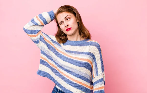 Genç, güzel bir kadın şaşkın ve kafası karışmış hissediyor, başını kaşıyor ve yan tarafa bakıyor.