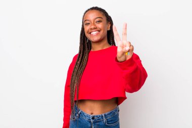 afro pretty woman smiling and looking happy, carefree and positive, gesturing victory or peace with one hand