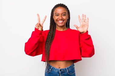 afro pretty woman smiling and looking friendly, showing number seven or seventh with hand forward, counting down