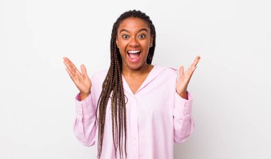 afro pretty woman looking happy and excited, shocked with an unexpected surprise with both hands open next to face