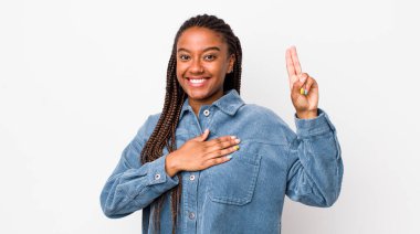 afro pretty woman looking happy, confident and trustworthy, smiling and showing victory sign, with a positive attitude