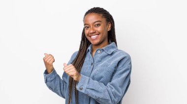 afro pretty woman smiling cheerfully and casually pointing to copy space on the side, feeling happy and satisfied