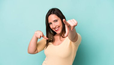 young adult pretty woman feeling happy and confident, pointing to camera with both hands and laughing, choosing you