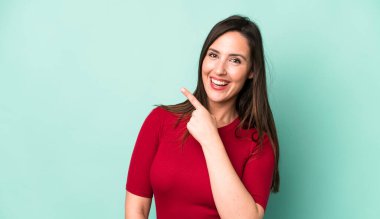young adult pretty woman looking excited and surprised pointing to the side and upwards to copy space