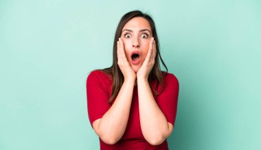 young adult pretty woman feeling shocked and scared, looking terrified with open mouth and hands on cheeks