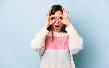 young adult pretty woman feeling shocked, amazed and surprised, holding glasses with astonished, disbelieving look