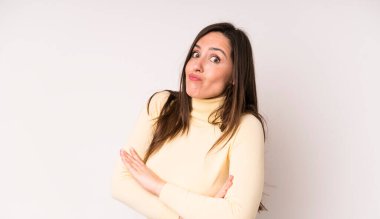 Genç ve güzel bir kadın omuz silkiyor, kafası karışık ve kararsız, kolları bağlı ve şaşkın bir şekilde bakıyor.