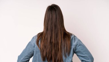 young adult pretty woman feeling confused or full or doubts and questions, wondering, with hands on hips, rear view