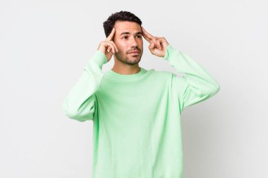young handsome hicpanic man feeling confused or doubting, concentrating on an idea, thinking hard, looking to copy space on side