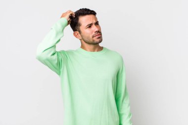 young handsome hicpanic man feeling puzzled and confused, scratching head and looking to the side