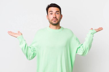 young handsome hicpanic man feeling puzzled and confused, doubting, weighting or choosing different options with funny expression