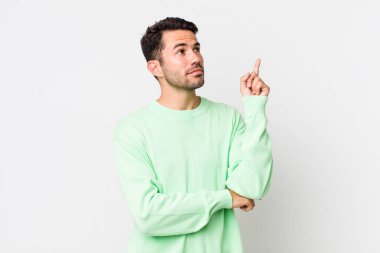 young handsome hicpanic man smiling happily and looking sideways, wondering, thinking or having an idea