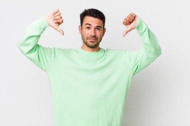 young handsome hicpanic man looking sad, disappointed or angry, showing thumbs down in disagreement, feeling frustrated