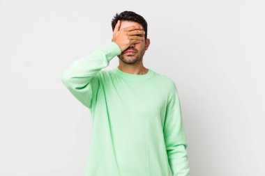 young handsome hicpanic man covering eyes with one hand feeling scared or anxious, wondering or blindly waiting for a surprise