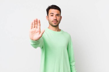 young handsome hicpanic man looking serious, stern, displeased and angry showing open palm making stop gesture