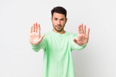 young handsome hicpanic man looking serious, unhappy, angry and displeased forbidding entry or saying stop with both open palms