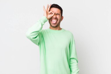 young handsome hicpanic man smiling happily with funny face, joking and looking through peephole, spying on secrets