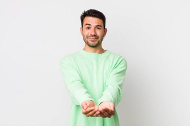 young handsome hicpanic man smiling happily with friendly, confident, positive look, offering and showing an object or concept