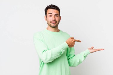 young handsome hicpanic man smiling, feeling happy, carefree and satisfied, pointing to concept or idea on copy space on the side