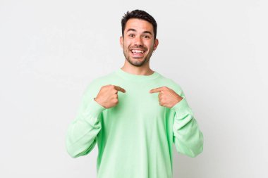 young handsome hicpanic man feeling happy, surprised and proud, pointing to self with an excited, amazed look