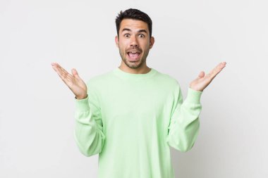 young handsome hicpanic man feeling happy, excited, surprised or shocked, smiling and astonished at something unbelievable