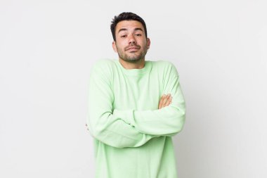 young handsome hicpanic man shrugging, feeling confused and uncertain, doubting with arms crossed and puzzled look