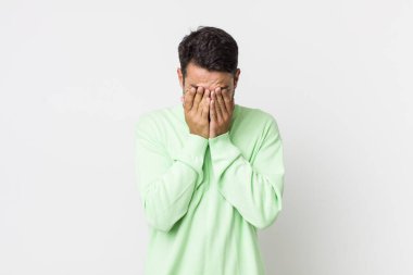 young handsome hicpanic man feeling sad, frustrated, nervous and depressed, covering face with both hands, crying