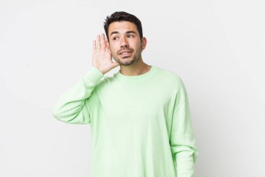 young handsome hicpanic man smiling, looking curiously to the side, trying to listen to gossip or overhearing a secret