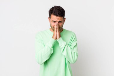 young handsome hicpanic man feeling worried, hopeful and religious, praying faithfully with palms pressed, begging forgiveness