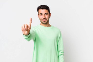 young handsome hicpanic man smiling and looking friendly, showing number one or first with hand forward, counting down