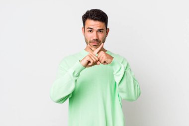 young handsome hicpanic man looking serious and displeased with both fingers crossed up front in rejection, asking for silence