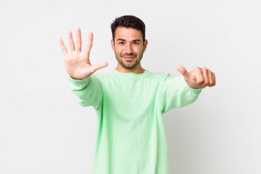 young handsome hicpanic man smiling and looking friendly, showing number six or sixth with hand forward, counting down