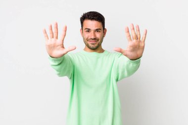 young handsome hicpanic man smiling and looking friendly, showing number ten or tenth with hand forward, counting down