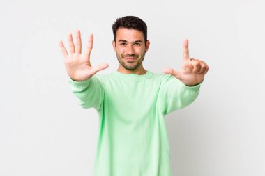 young handsome hicpanic man smiling and looking friendly, showing number seven or seventh with hand forward, counting down