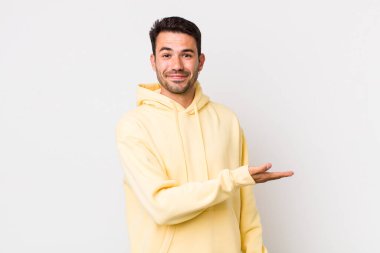 young handsome hicpanic man smiling cheerfully, feeling happy and showing a concept in copy space with palm of hand